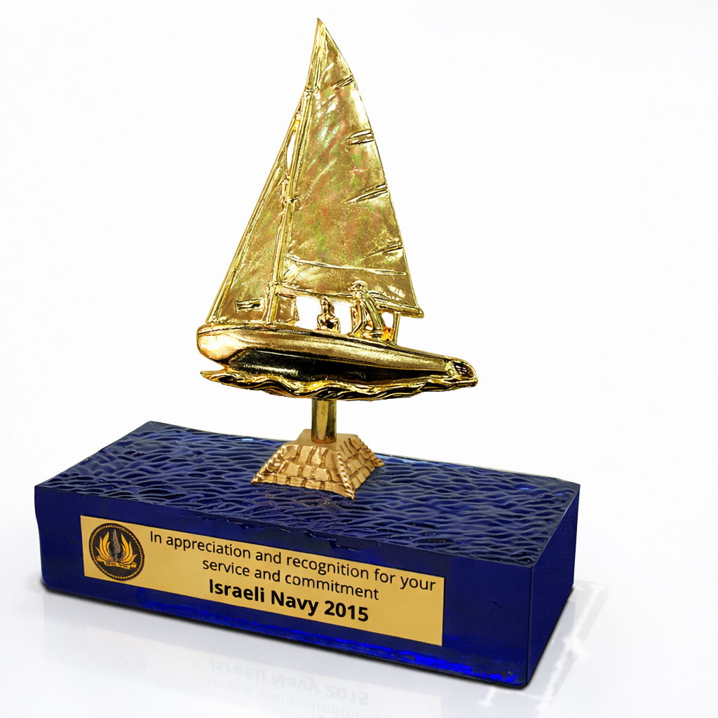 מגן הוקרה לחיל הים עם פסלון מפרשית זהב על בסיס זכוכית כחולה בטקסטורת גלים ופלטת הקדשה אישית.